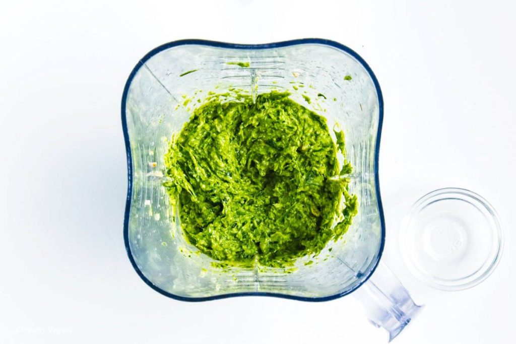 A mixture of garlic scapes, walnuts, olive oil, lemon juice, basil leaves and salt in a food processor.