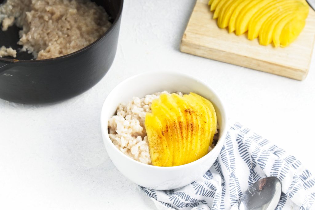 Vegan rice pudding topped with sliced ripe mango  in a small white bowl.