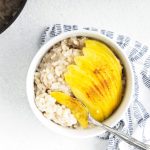 Vegan Rice Pudding topped with ripe mango placed in a small white bowl and a spoonful of rice pudding with ripe mango.